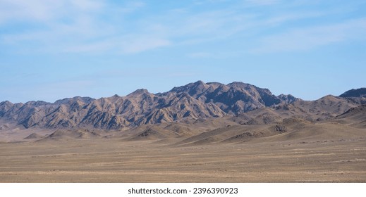 a wide desert with a vast, flat plain stretches out, covered with sparse, dry vegetation and rolling hills, leading up to a rugged mountain range with the light of the sun creating a play of shadows. - Powered by Shutterstock
