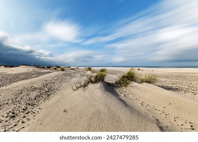 Wide deserted Baltic Sea beach in sunny windy weather, wind-moving grass and sand dunes, motion traces of clouds by long exposure, dark clouds, Poland, Baltic Sea, Slowinski Park Narodowy - Powered by Shutterstock