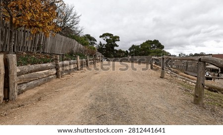 A wide dirt walking path lined with rustic log and picket fences under overcast skies.