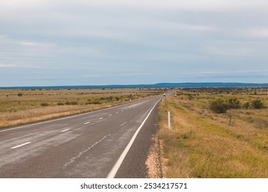 The wide, empty road stretches across the Queensland Outback, surrounded by endless grasslands and distant hills under a cloudy sky. Perfect for an adventurous road trip. - Powered by Shutterstock