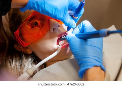 A Wide Eyed Girl Sits In A Dental Chair Getting Her Teeth Cleaned.  She Is Wearing Big, Eye Shielding, Orange Glasses.