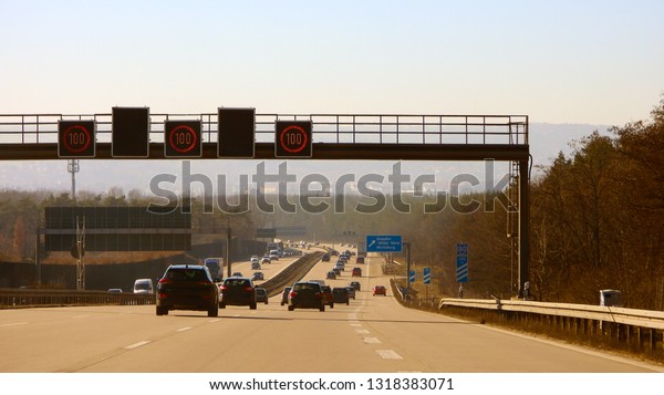 Wide german\
autobahn, speed highway across all big cities in Germany. Road\
traffic with colorful cards, concrete asphalt, road signs and\
dividing line lighted by sun in the\
sunset