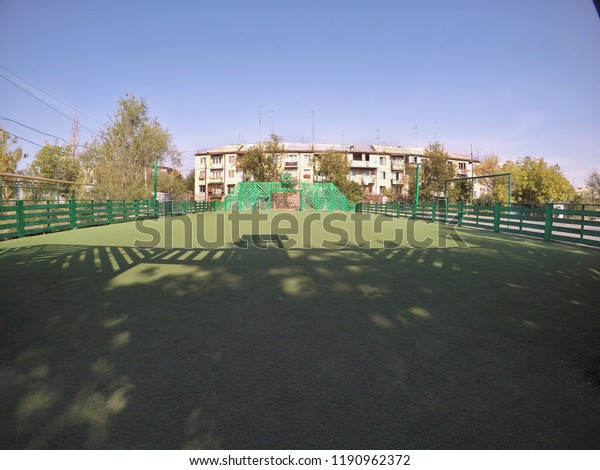 wide Green football and basketball play ground\
with wooden walls near the\
homes