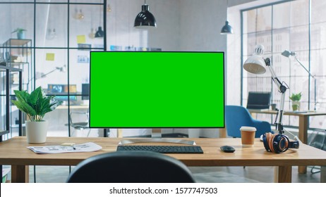 Wide Green Mock-up Screen Desktop Computer Standing on the Desk in the Modern Creative Office. In the Background Bright Creative Loft for Developers and Designers where Professional Working. - Powered by Shutterstock