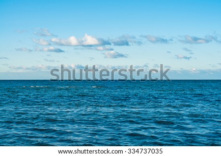 Wide horizon above wavy dark ocean at slightly clouded sky