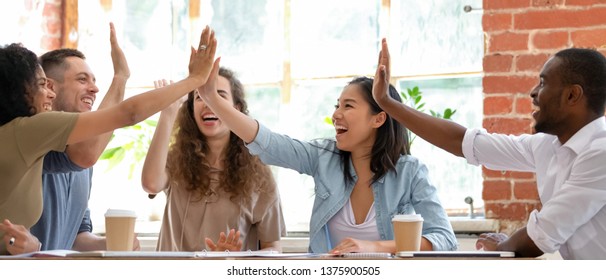 Wide horizontal image multicultural cheerful businesspeople sitting together at meeting giving high five gesture feels excited happy, showing team spirit, celebrating victory goal achievement concept - Shutterstock ID 1375900505