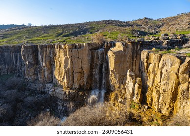 Wide landscape of basalt cliffs with a small waterfall in Tavaksay canyon, Tashkent Region, Uzbekistan.