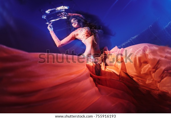 wide and low angle shot of belly\
dancer with in orange outfit performing with fire at\
night