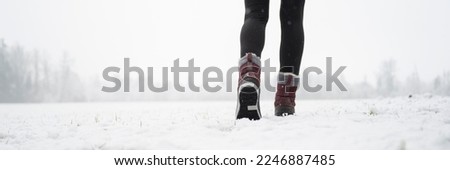 Wide low angle view image of female legs in winter boots walking in snow covered nature.