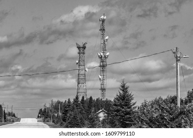 A Wide Monochrome View Of Service Provider Infrastructure In A Canadian Town. With Cell Site Tower, Steel Pylon, Street Furniture, Overhead Cables