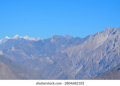 Wide mountain range landscape in Gilgit Baltistan Pakistan with distant snowy peaks rocky ridges and clear blue sky.