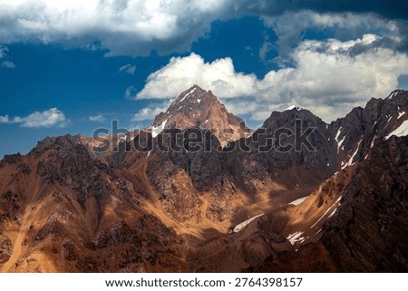 Wide mountain range panorama featuring Maloalmatinsky Peak. Dramatic lighting on rocky ridges and alpine terrain in Trans-Ili Alatau near Almaty.