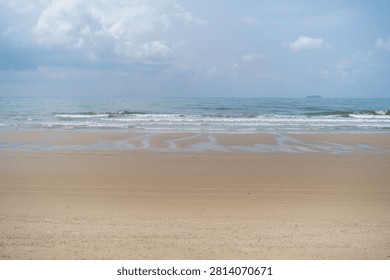 Wide open empty sandy beach with gentle sea waves and soft cloudy sky stretching to the horizon. Peaceful seascape concept