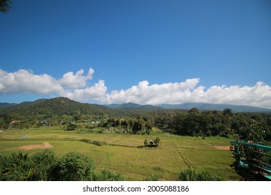 A Wide Open Field With Mountains And Blue Sky Background