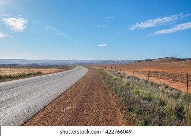 Wide Open Landscape In Western Australia With Roadway In Diminishing Perspective Under A Blue Sky With Minimal Clouds/Road Trip/Western Australia