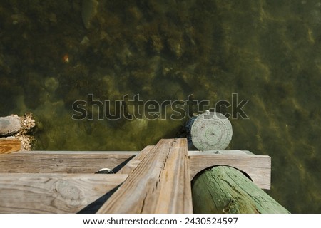 Wide Overhead looking down wood pilings of a pier dock towards shallow water. Shows grain of wood in afternoon sun. Wide view of clear calm bay water with room for copy and no people. Shells on wood.