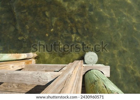 Wide Overhead looking down wood pilings of a pier dock towards shallow water. Shows grain of wood in afternoon sun. Wide view of clear calm bay water with room for copy and no people. Shells on wood.