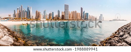 Wide panorama of the Persian Gulf with sandy beach and Bluewaters Island with the worlds famous largest Ferris wheel Dubai Eye and numerous skyscrapers with hotels and residences