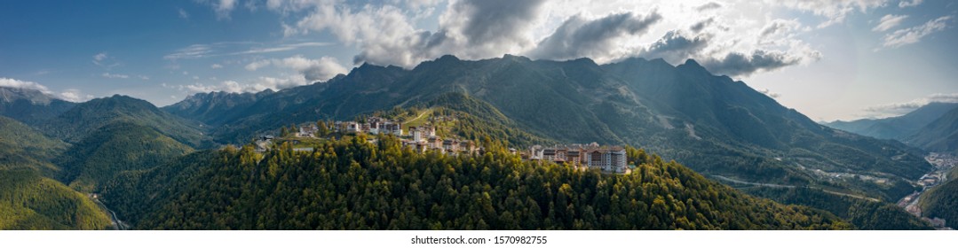 Wide panorama of Rosa Khutor mounrain ski resort of Russia in sunny evening; olympic village surrounded by mountain ranges, valleys; summer winter widely known tourist destination for hiking, trekking