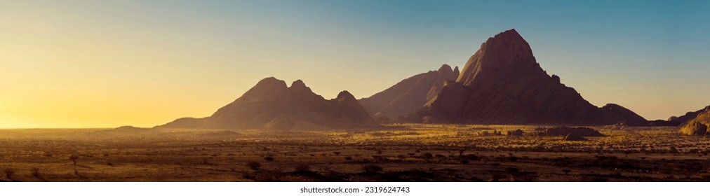 Wide panorama of a stone desert at sunrise in haze  of soft sunlight, mountain landscape of Spitzkoppe hills, Namibia. Travel to wildlife of Africa, extreme tour, adventures to wilderness.  - Shutterstock ID 2319624743