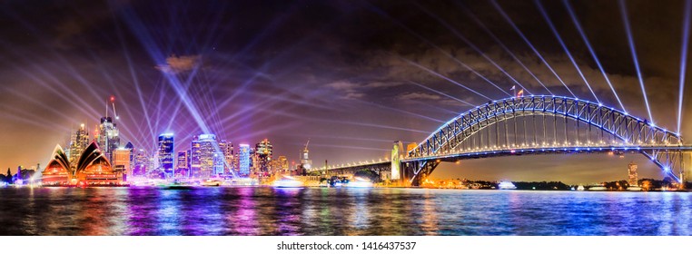 WIde panorama of Sydney city CBD landmarks and high-rise office buildings on waterfront of Harbour with the Sydney harbour bridge at Vivid Sydney light show illumination.