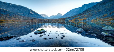 Wide panorama of Tahtarjavr lake with transparent water, rocky bottom and distant mountains reflected in still morning waters, Hibiny mountains above the Arctic circle, Russia