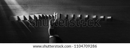 Wide panorama top view of businessman stopping falling blocks on table, monochrome image.