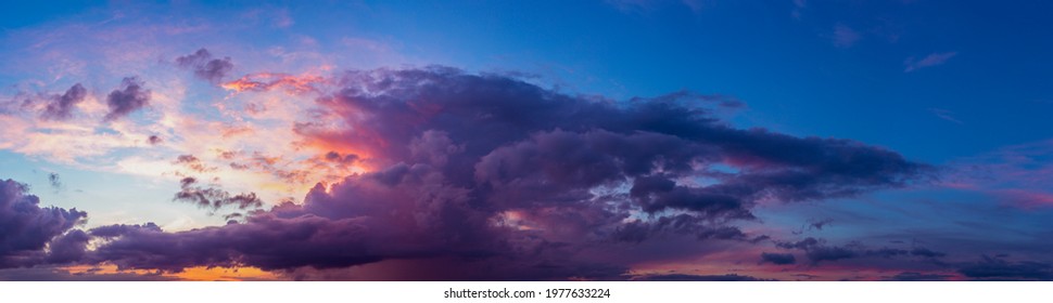 Wide panorama with vibrant blue sky and dramatic sunset contrasting colors of yellow, red and orange touching the cumulus cloud. Weather conditions. Wallpaper poster.