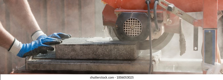 Wide Panorama View Of A Building Contractor Using An Angle Grinder Outdoors To Cut Through A Paving Slab Or Brick In A Cloud Of Dust.