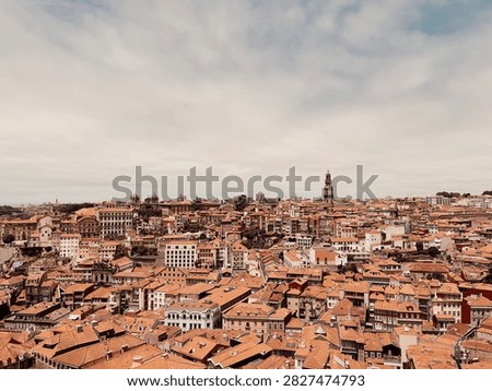 A wide panoramic high-angle view over the historic old town of Porto, Portugal, showcasing a dense cityscape of traditional terracotta tiled roofs under an overcast sky, with the iconic Clerigos Tower (Torre dos Clerigos) rising above the skyline