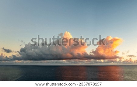 Wide panoramic view of cumulus clouds lit by the rising sun over the ocean off north coast of Kauai