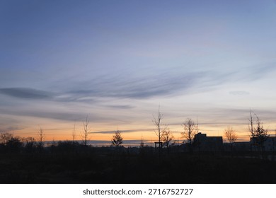 Wide panoramic view of a dramatic sunset sky with wispy purple and orange clouds over a dark suburban horizon, tranquil evening landscape, peaceful twilight scene in a park.