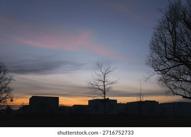 Wide panoramic view of a dramatic sunset sky with wispy purple and orange clouds over a dark suburban horizon, tranquil evening landscape, peaceful twilight scene in a park.