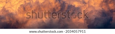 a wide panoramic view of the gloomy orange-purple stormy sunset sky with cumulus clouds. atristic moody image for dramatic design or decoration