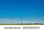 Wide panoramic view of high voltage transmission towers and overhead power lines above rural farmland, with open blue sky copy space for energy, infrastructure and agriculture concepts.