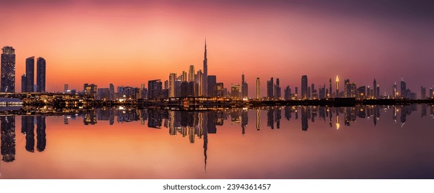 Wide panoramic view of the illuminated skyline of Dubai Business bay with reflections of the modern skyscrapers in the water during dusk time, UAE - Powered by Shutterstock