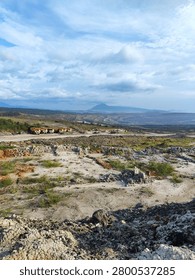 Wide panoramic view of a massive open-pit coal mining site with a fleet of heavy yellow dump trucks parked on the terrace. A scenic mountain and cloudy sky are visible in the background.