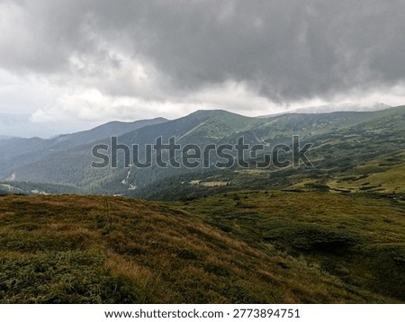 Wide panoramic view of rolling green slopes and hiking trails of Chornohora range. Ominous grey clouds and mist touch peaks. Powerful atmosphere of wild nature.