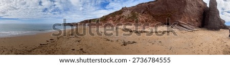 Wide panoramic view of a sandy beach with red coastal cliffs and calm sea under a partly cloudy sky.