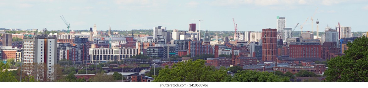 a wide panoramic view showing the whole of leeds city center with towers apartments roads and commercial buildings against a blue sky