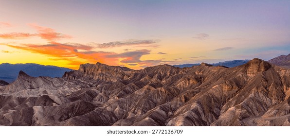Wide panoramic view of sunset light illuminating the eroded badlands at Zabriskie Point in Death Valley National Park, California. Warm golden hour tones highlight the layered desert landscape, ridges, and dramatic textures, creating a striking natural scene ideal for travel, tourism, and nature themes.