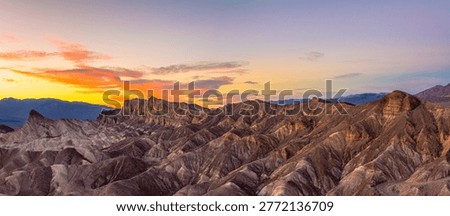 Wide panoramic view of sunset light illuminating the eroded badlands at Zabriskie Point in Death Valley National Park, California. Warm golden hour tones highlight the layered desert landscape, ridges, and dramatic textures, creating a striking natural scene ideal for travel, tourism, and nature themes.