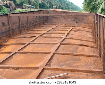 Wide perspective view of an empty rusty steel barge cargo hold with iron grid structure