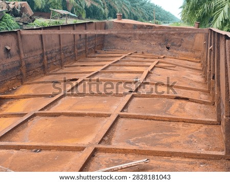 Wide perspective view of an empty rusty steel barge cargo hold with iron grid structure