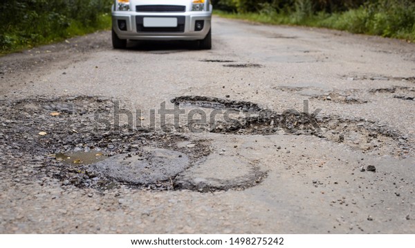 Wide picture of a car\
approaching part of a road in poor condition with lot of holes and\
chuckholes