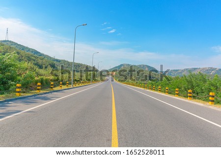 Wide road through the mountains under the blue sky and white clouds