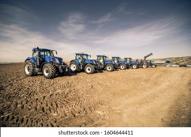 Wide row of blue modern tractors standing right next to each other in the field during sunny autumn day. Big tractor dealership event. 