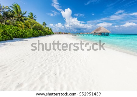 Wide sandy beach on a tropical island in Maldives. Coconut palms and water lodge on Indian Ocean.