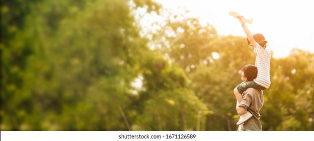 Wide Screen Of Asian Father Put His Son On His Shoulder To Play Paper Plane, Spending Time Together At Park In Autumn Afternoon Sunlight, The Concept Father's Day, Daddy Hero, Family Background.