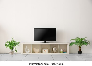 Wide Screen TV On White Stand Near Light Wall